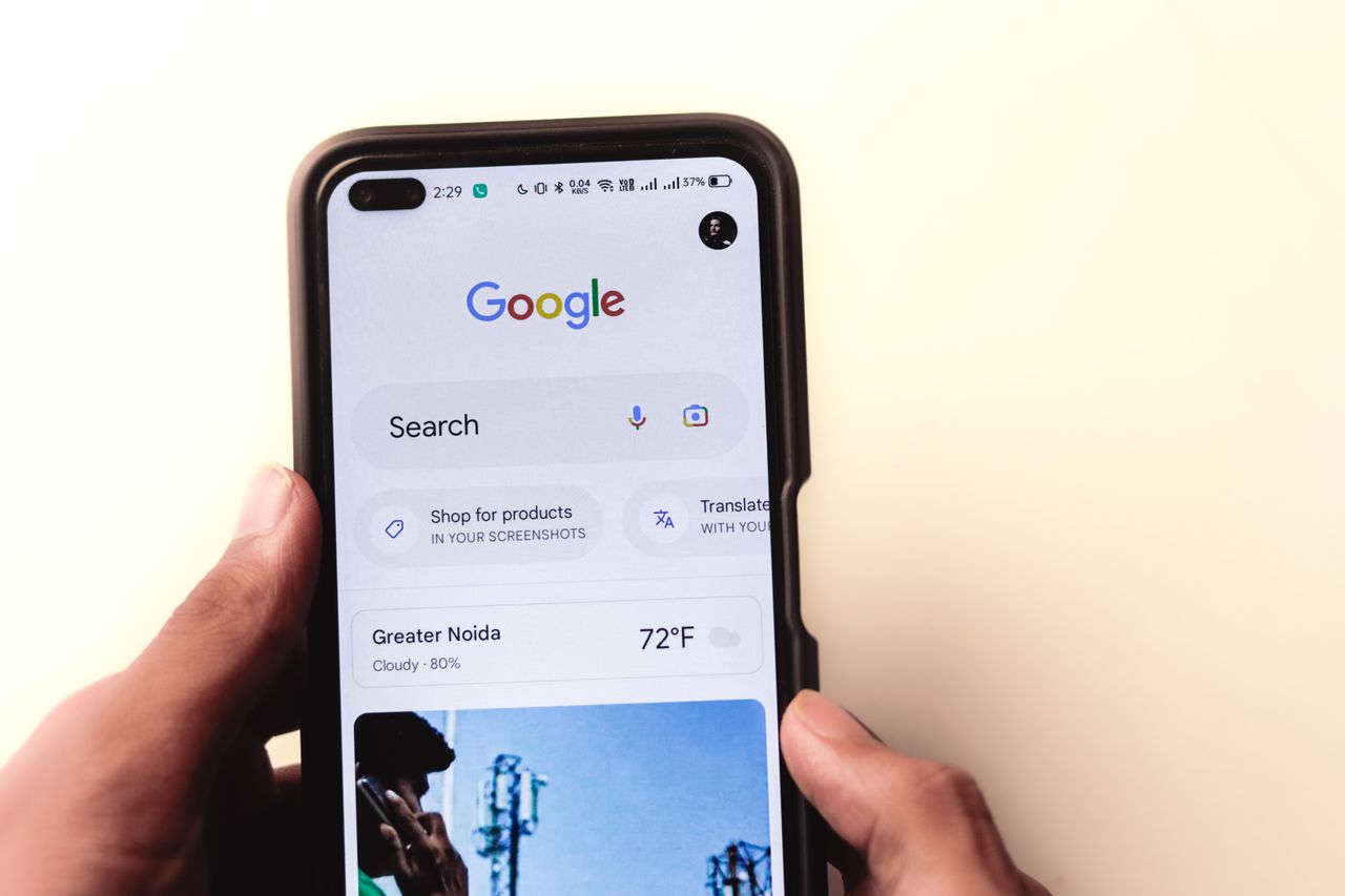 A close-up view of a hand holding a smartphone, with a Google search shown on the screen.